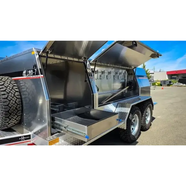 A close-up of the Lynx 7, a rugged off-road utility trailer with large tires, open storage for wildfire equipment Canada, pull-out drawers, and a metallic finish, parked outdoors on a sunny day.