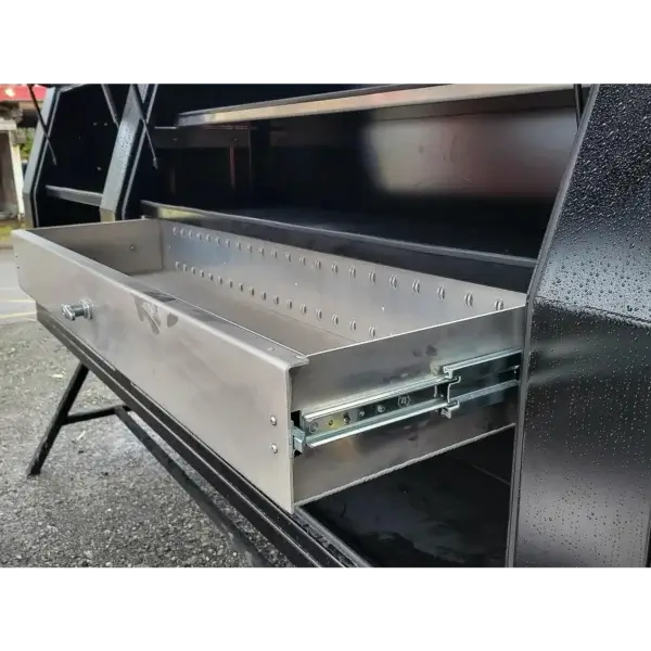 A close-up of a metal drawer partially pulled out from the Wildcat 1150 black storage cabinet, revealing its sliding mechanism. Used for wildfire equipment, the cabinet is shown outdoors with visible water droplets on its surface.