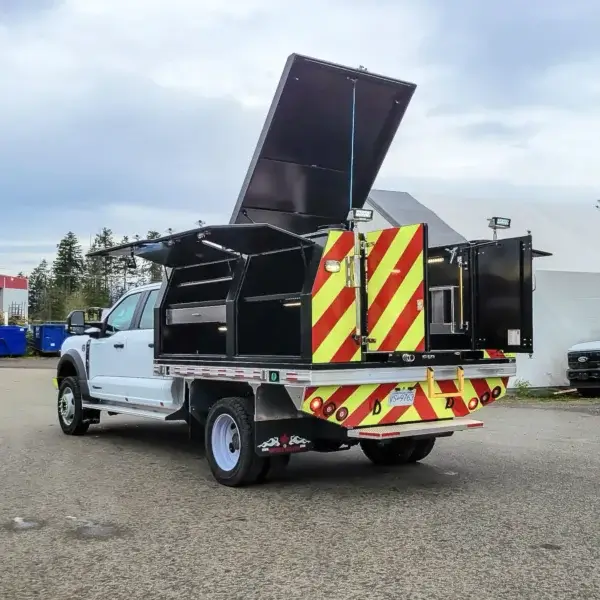 A Wildcat 950 white utility truck with an open flatbed and black storage compartments for wildfire gear, rear doors featuring red and yellow reflective stripes, is parked outdoors near tents and trees.