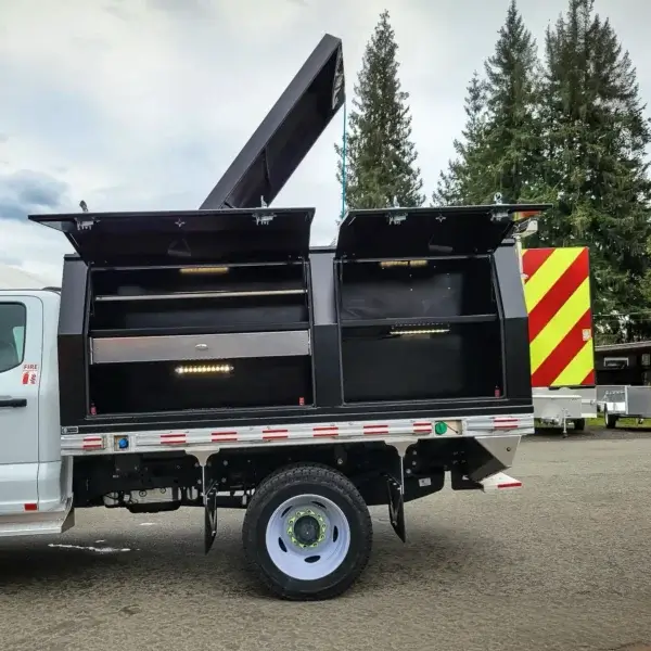 The Wildcat 950 utility truck is shown with side compartments and top hatch open, revealing spacious storage for wildfire gear used by Canadian firefighters. It’s parked outdoors among trees and other vehicles, with bright safety stripes visible in back.
